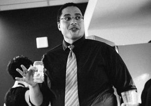 Kevin is backstage in a nice tie and black shirt drinking a bubbly water. Unlike his usual stoic self, he's smiling which is why we chose this picture for him to go with his bio..