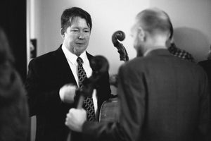 Skip is backstage wearing a suit and tie, looking empathetic and serious, probably talking to Doug who is blurred in the foreground. 