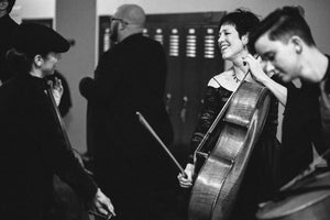 Diane is backstage, smiling and looking powerful holding her cello up while tuning it and carrying on a conversation at the same time.