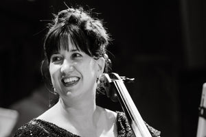 Nancy is smiling quite genuinely, full of life in her eyes, looking to the side, away from her cello. She's wearing a fancy dress, but not typical symphony black.  